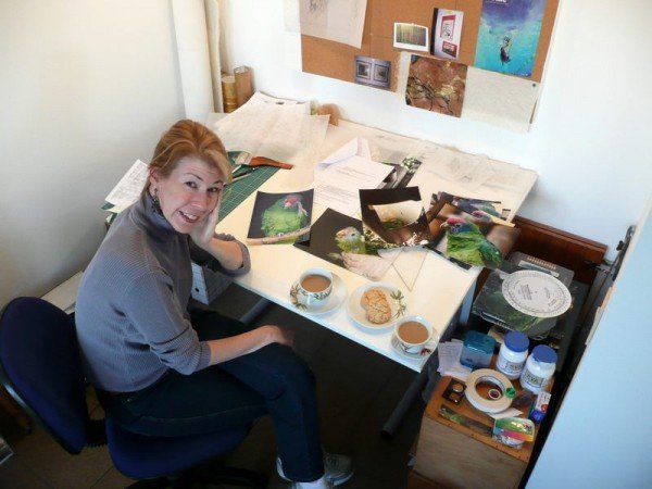 Kitty Harvill at her desk with her feathered muses